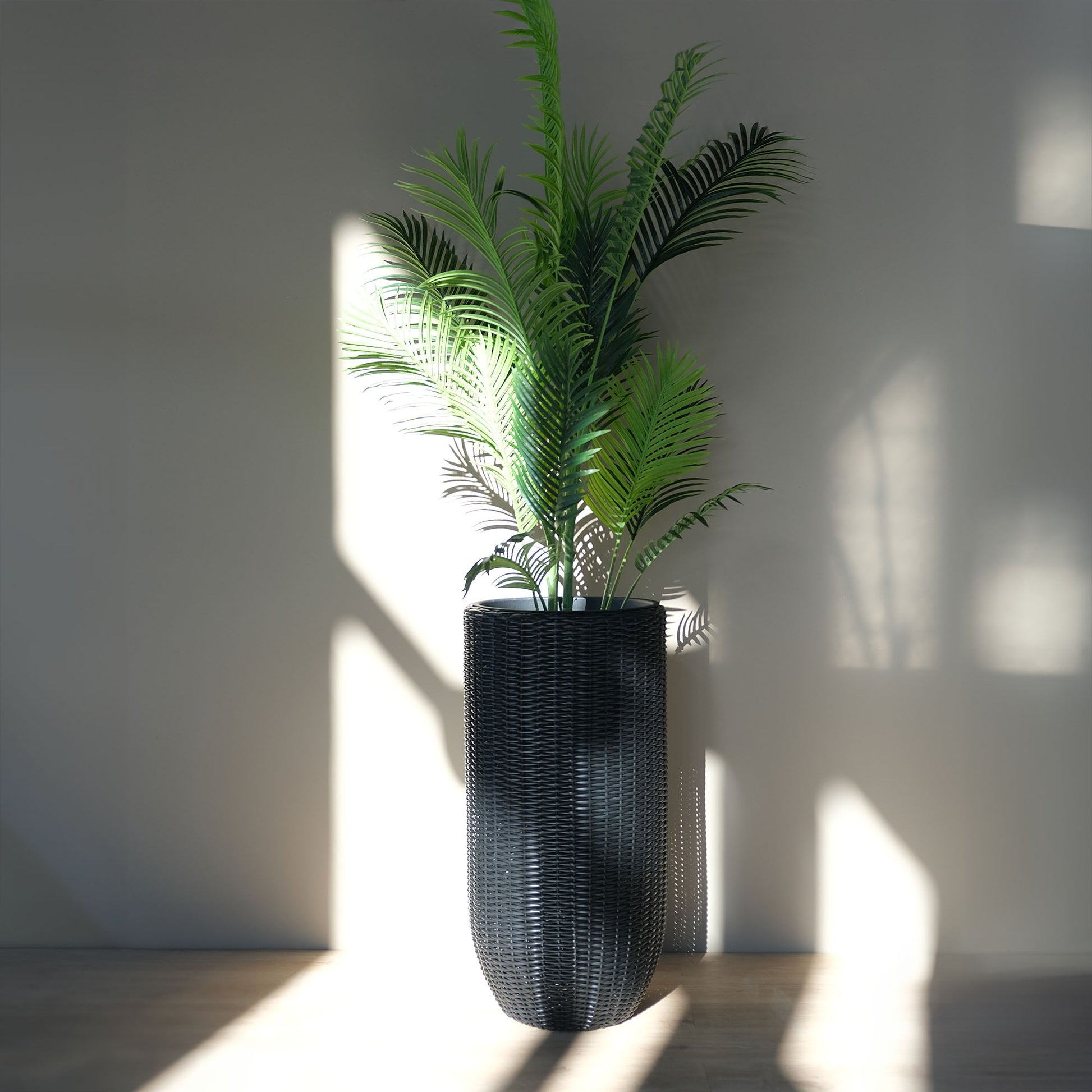 Tall black rattan planter with a tropical faux-palm tree