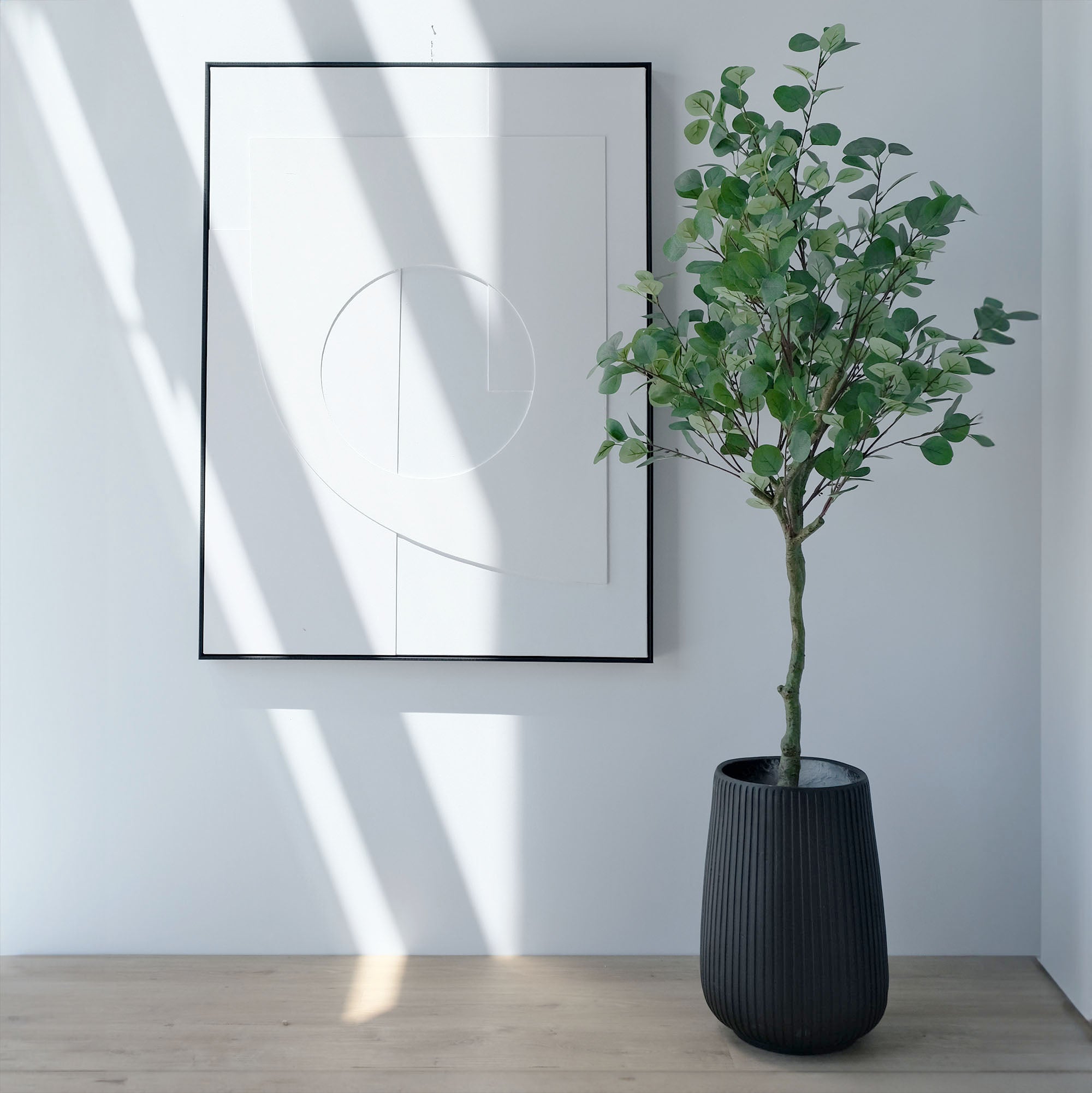 Faux-eucalyptus  plant in a black planter next to art