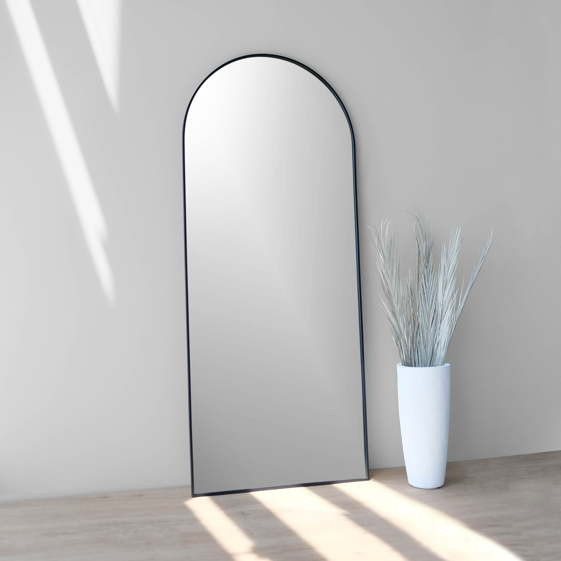 Side view of 30x70-inch iron black arch mirror leaning against wall
