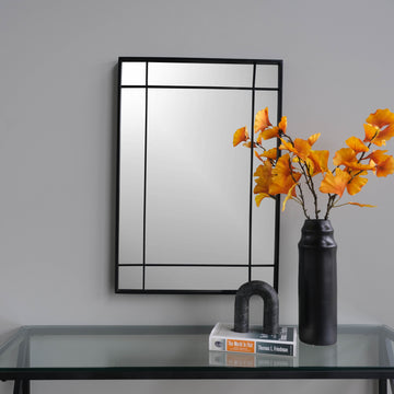 decorative mirror with black lines on top of a console table and a flower