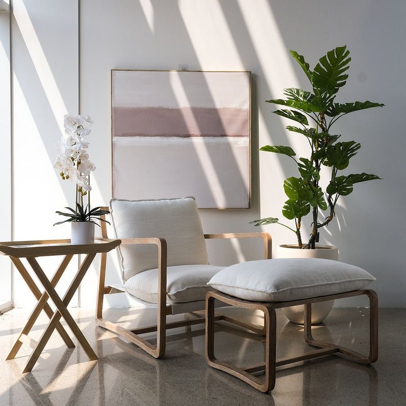 Neutral theme room setting: canvas art, neutral accent chair and a monstera plant in a planter